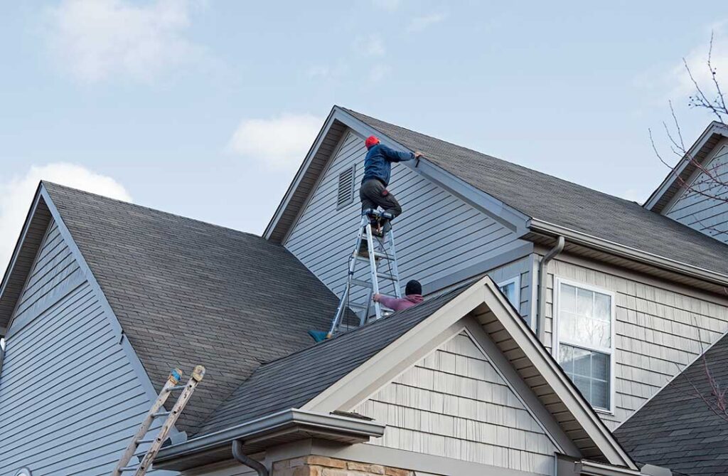 A worker installing asphalt shingles and underlayment on a residential pitched roof.