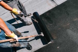 Separated asphalt shingles and metal roofing pieces sit under a secured tarp beside a cleanup area.